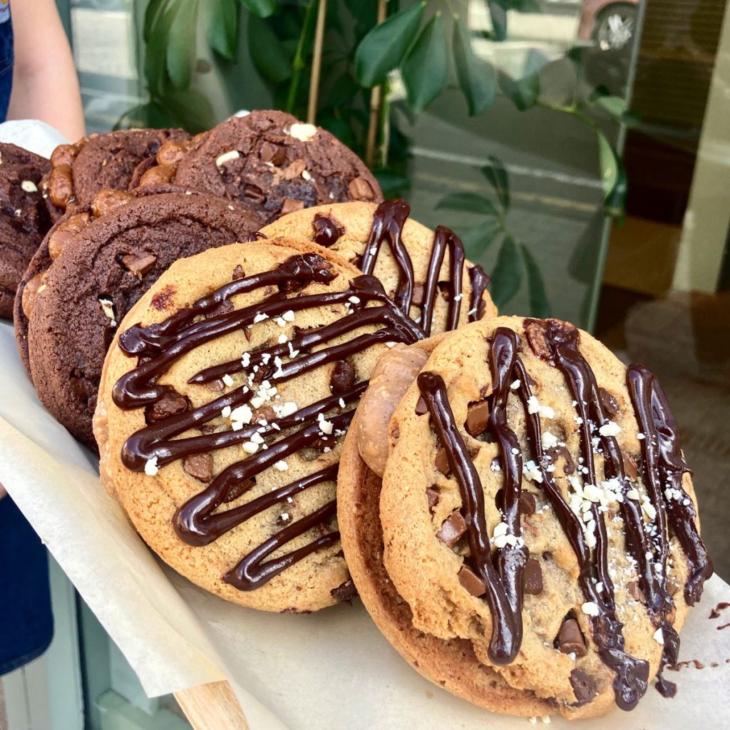 Nutella and triple chocolate cookie sandwiches stacked on a plate. They are filled with a chocolate fondant drizzled in dark chocolate and sprinkled in white chocolate.